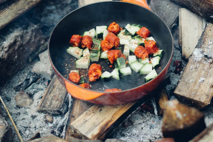 Vegetables and sausage cooking in a skillet over campfire coals
