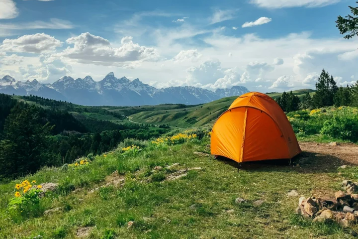 Orange dome tent pitched in a green mountain meadow