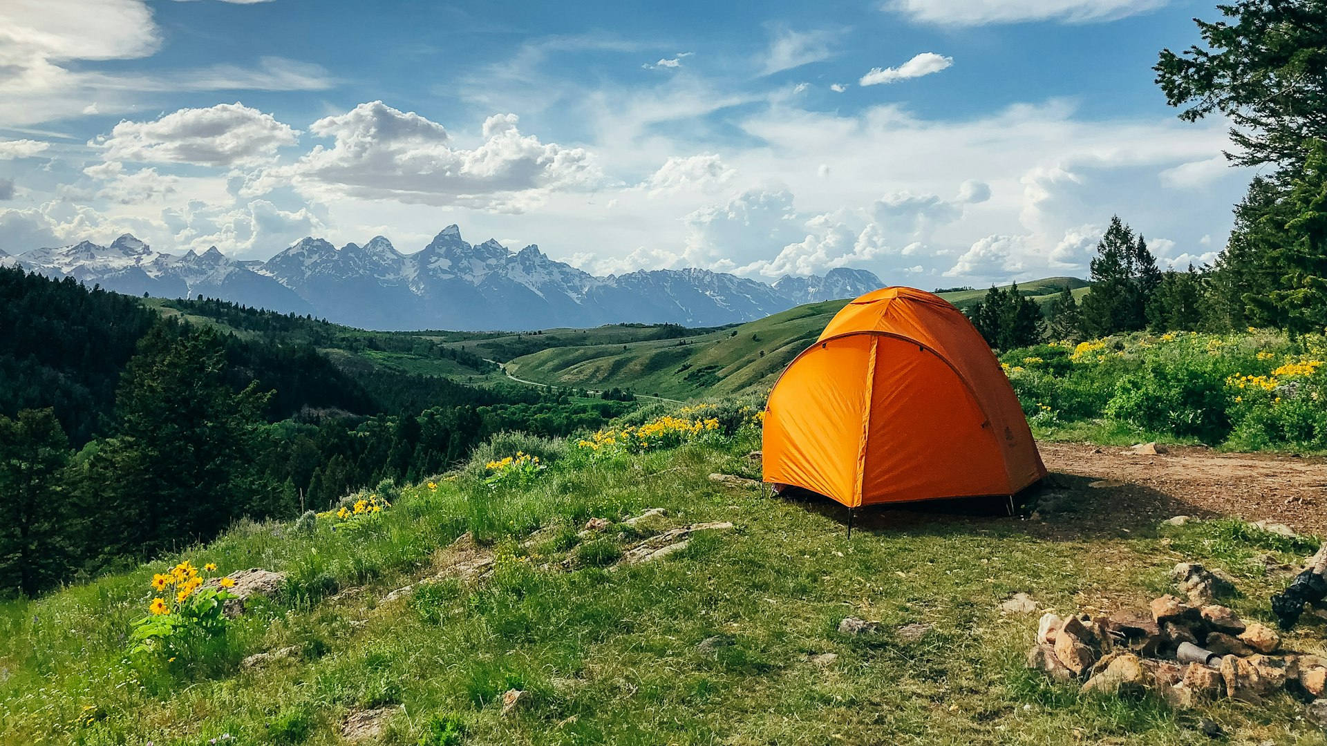 Orange dome tent pitched in a green mountain meadow
