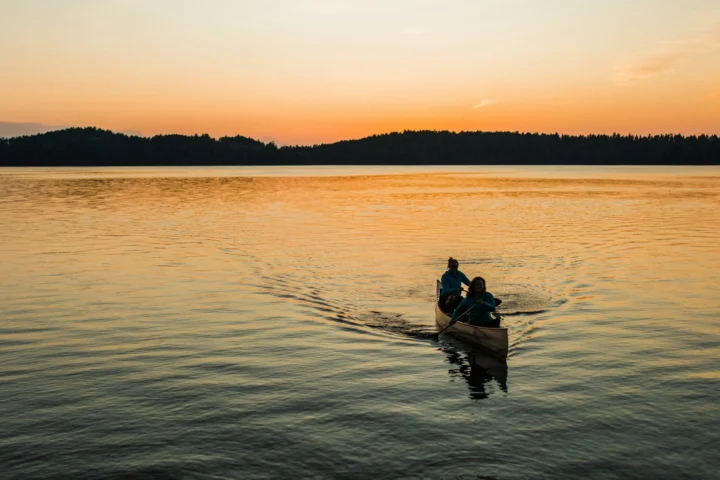 Two paddlers in a canoe crossing a calm lake at sunset