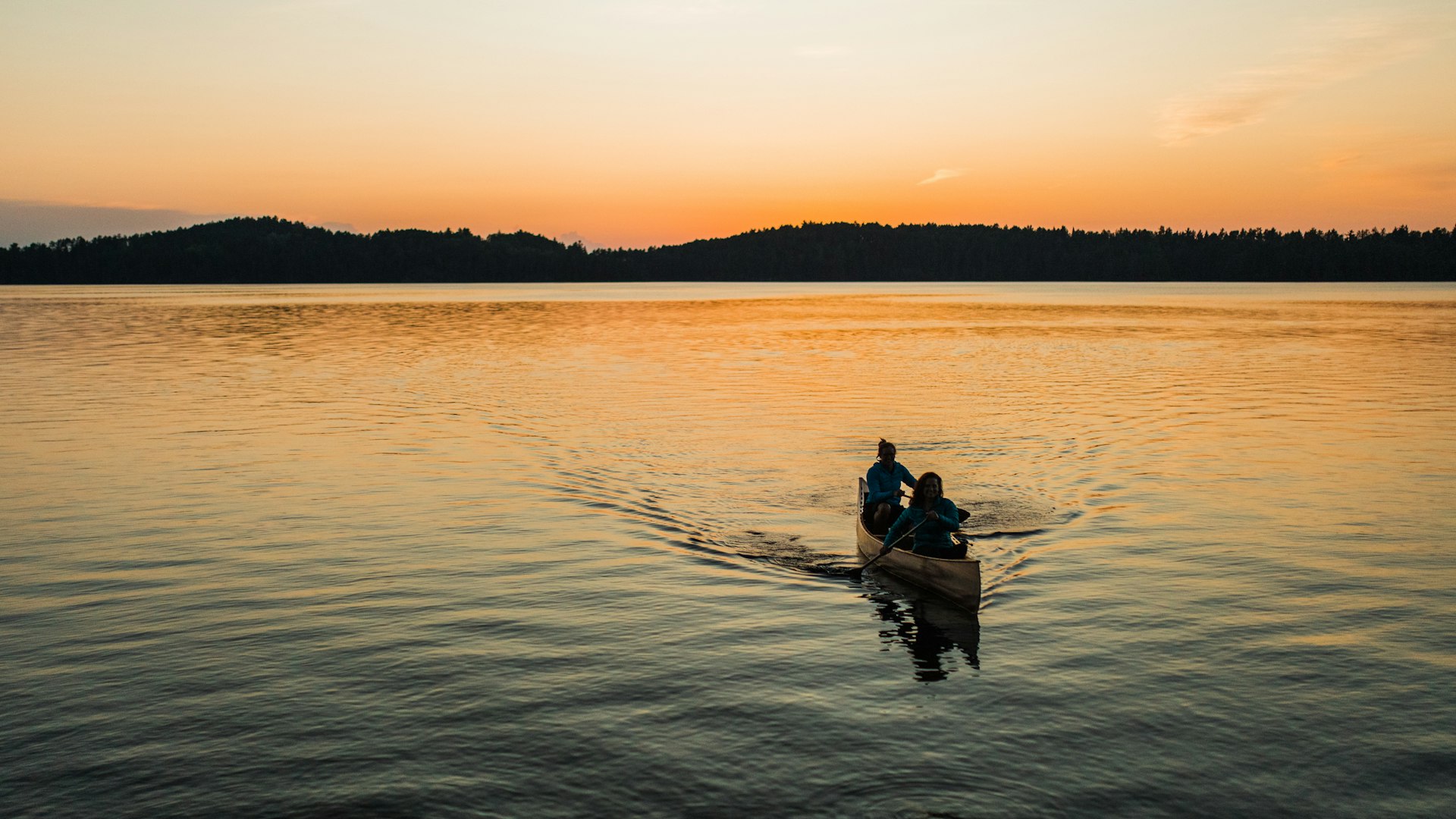 Two paddlers in a canoe crossing a calm lake at sunset