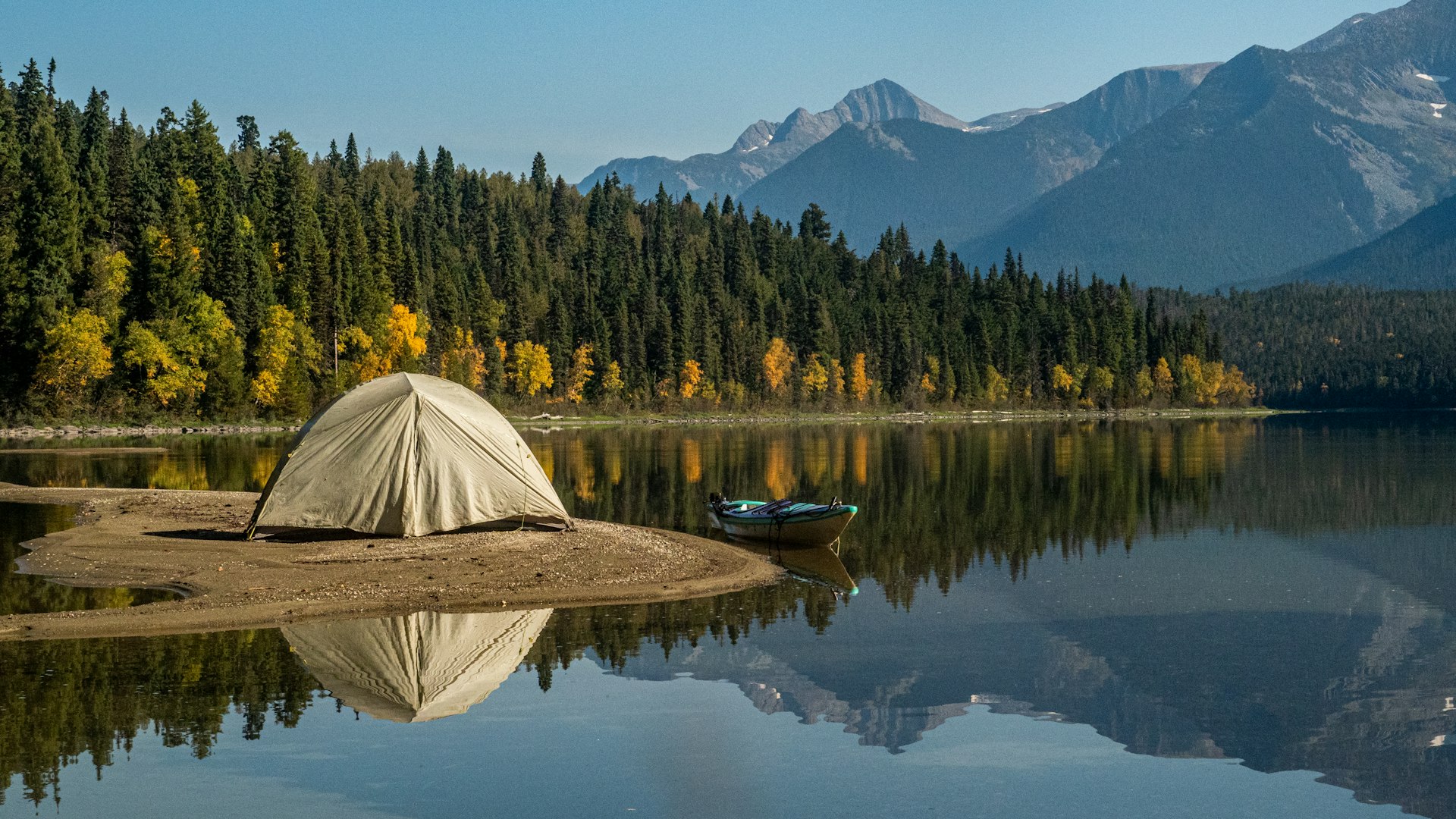 Tent on a small beach at a mountain lake with a canoe beside it