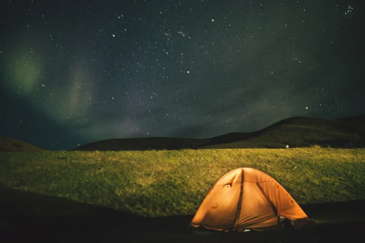 Lit tent under a night sky with northern lights on the horizon