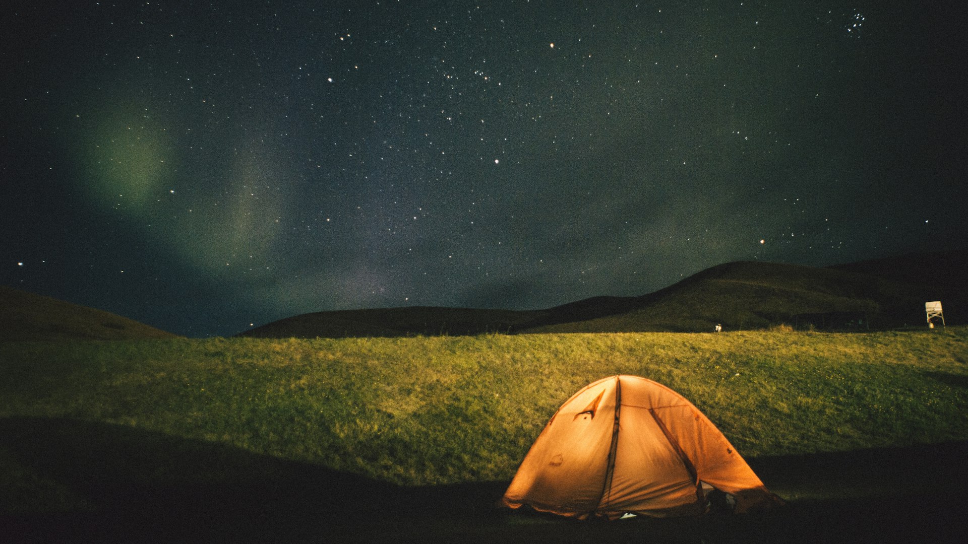 Lit tent under a night sky with northern lights on the horizon