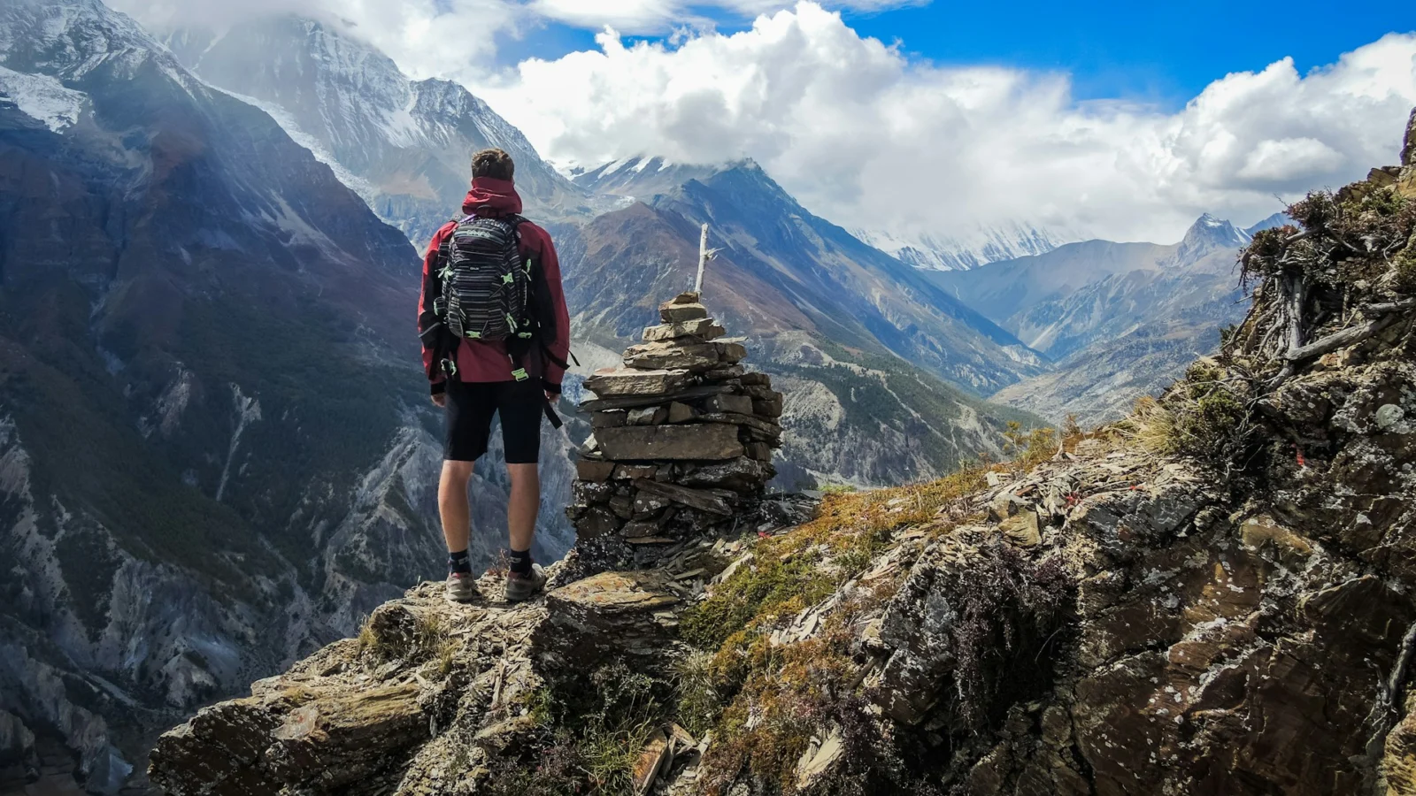 Hiker with a daypack standing by a cairn above a mountain valley