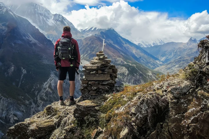 Hiker with a daypack standing by a cairn above a mountain valley