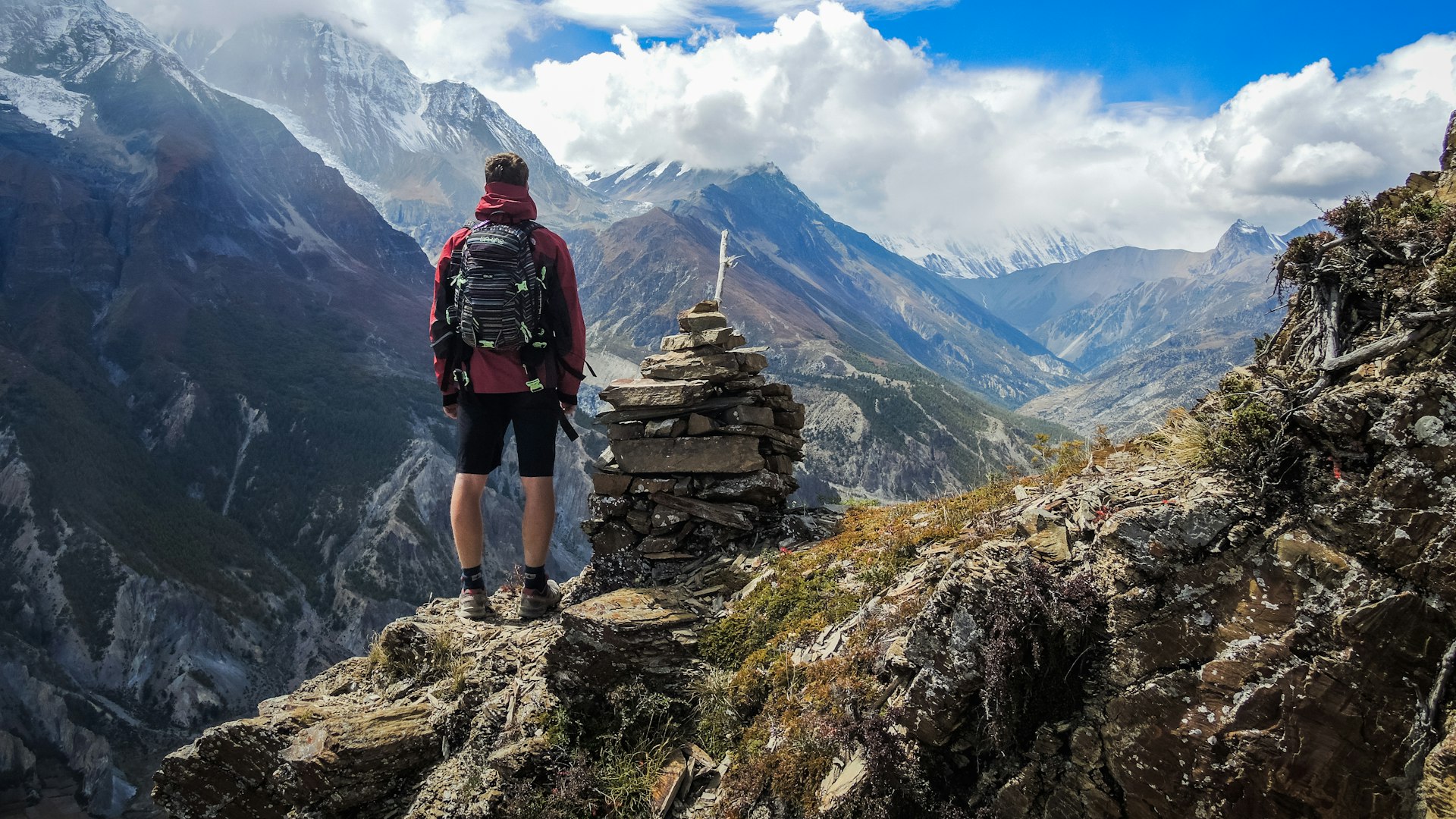 Hiker with a daypack standing by a cairn above a mountain valley