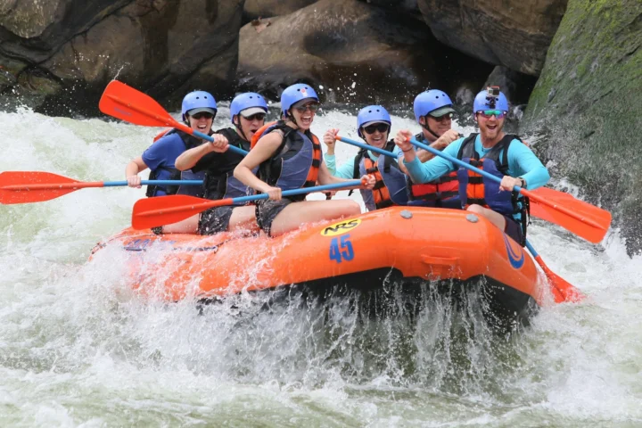 Rafting crew in helmets paddling an orange raft through whitewater